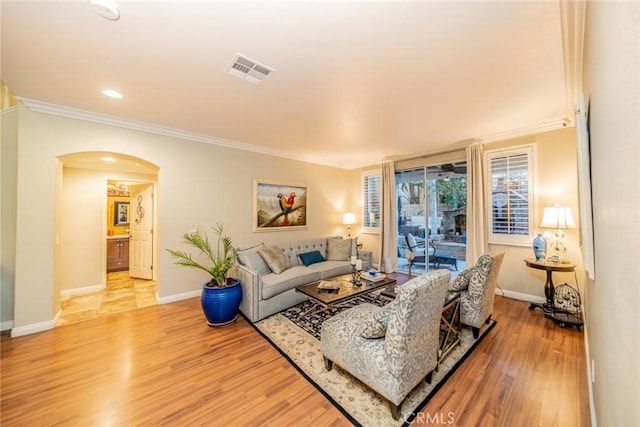 living area with arched walkways, light wood-type flooring, visible vents, and crown molding