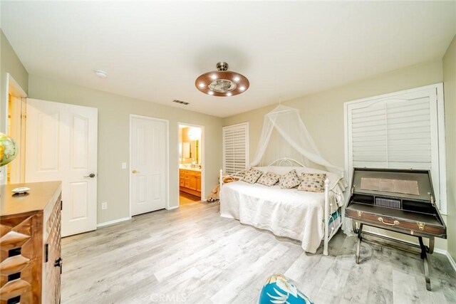 bedroom with light wood-style floors, visible vents, baseboards, and ensuite bathroom