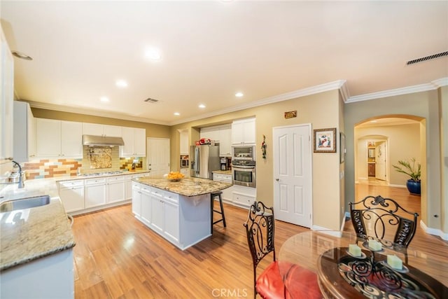 kitchen featuring arched walkways, a kitchen breakfast bar, stainless steel appliances, under cabinet range hood, and a sink