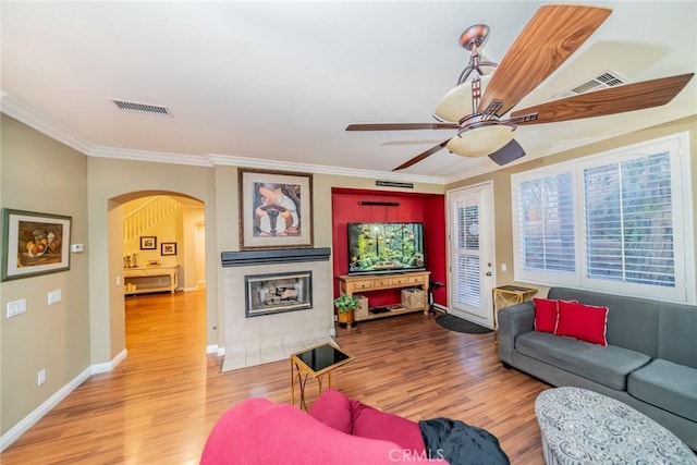 living area featuring visible vents, arched walkways, wood finished floors, and ornamental molding