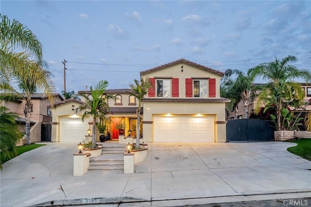 mediterranean / spanish home with driveway, a tiled roof, a gate, and stucco siding