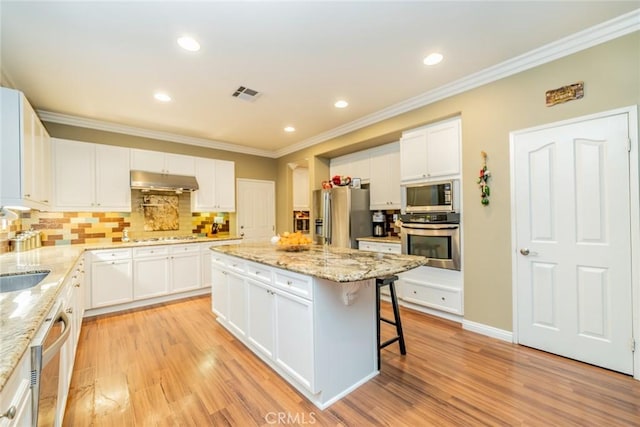 kitchen with visible vents, appliances with stainless steel finishes, a breakfast bar area, crown molding, and under cabinet range hood