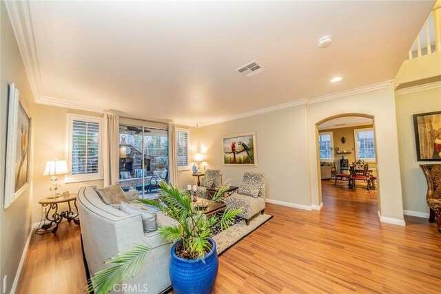 living area featuring light wood-style floors, arched walkways, visible vents, and ornamental molding