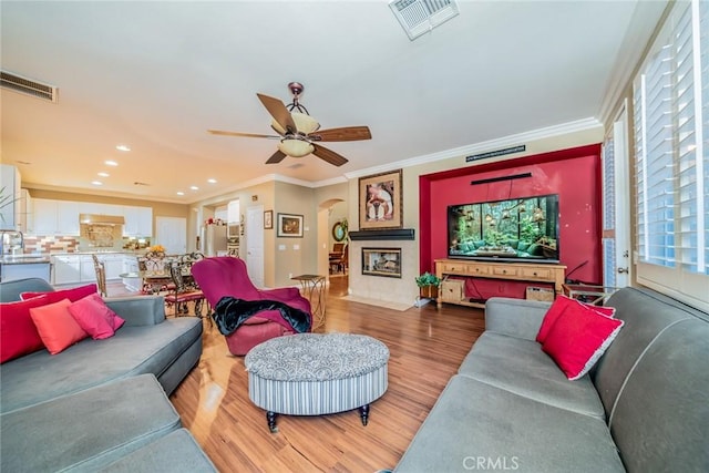 living area with crown molding, visible vents, and light wood-style floors