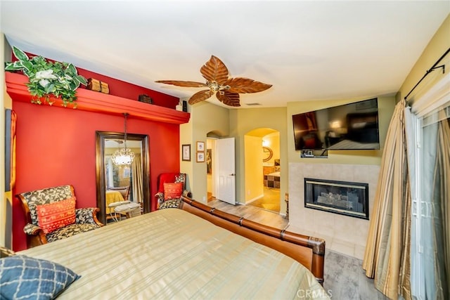 bedroom featuring a ceiling fan, arched walkways, a tiled fireplace, and wood finished floors