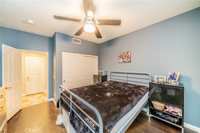 bedroom with wood finished floors, a ceiling fan, visible vents, baseboards, and a closet