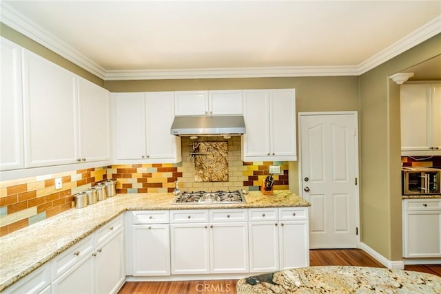 kitchen with light stone counters, under cabinet range hood, stainless steel gas cooktop, white cabinetry, and decorative backsplash