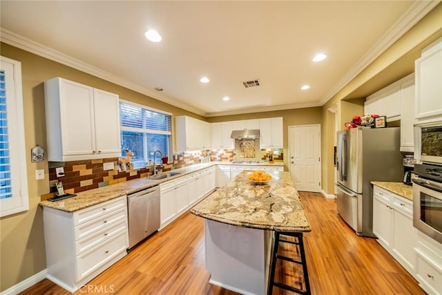 kitchen with under cabinet range hood, stainless steel appliances, a sink, visible vents, and a center island