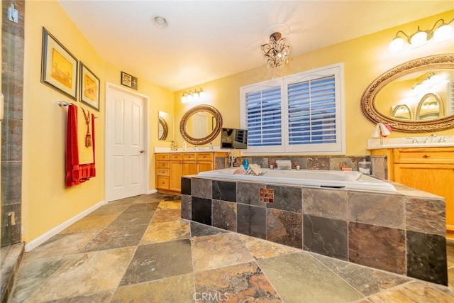 bathroom with vanity, a garden tub, stone tile flooring, and baseboards