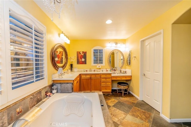 bathroom with double vanity, baseboards, a garden tub, stone finish flooring, and a sink