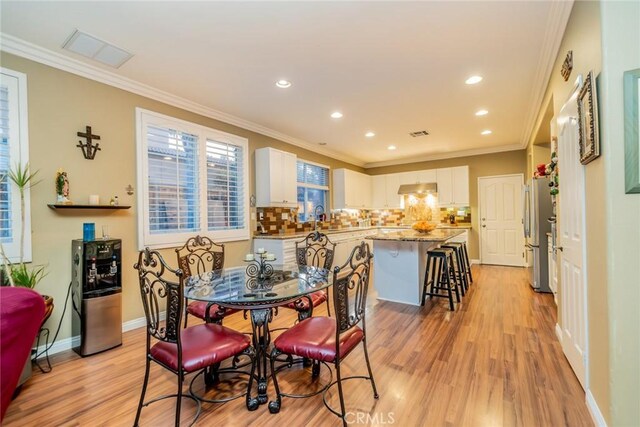 dining space featuring light wood-type flooring, baseboards, and crown molding