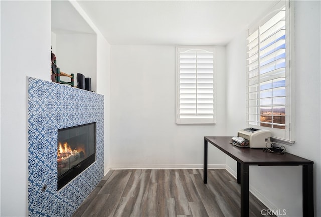 home office with baseboards, a tiled fireplace, and wood finished floors