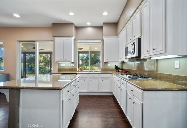 kitchen with white gas stovetop, white cabinets, stainless steel microwave, dark wood-type flooring, and a center island