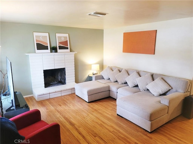 living room featuring a brick fireplace, visible vents, and light wood finished floors