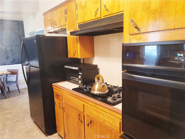 kitchen featuring a toaster, under cabinet range hood, backsplash, tile counters, and black appliances