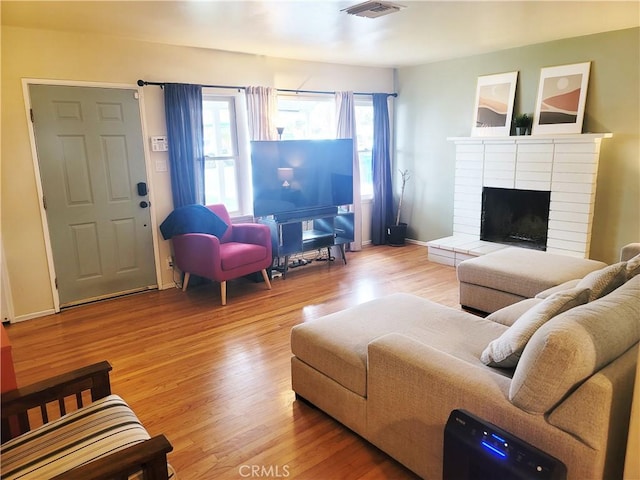 living area featuring a brick fireplace, visible vents, baseboards, and wood finished floors