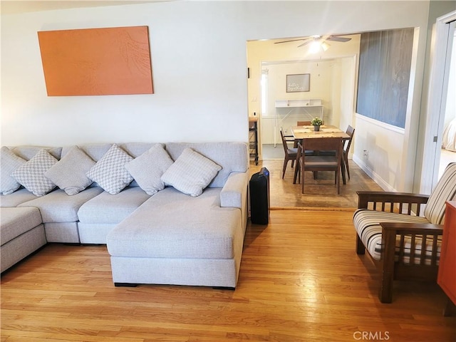 living area featuring a ceiling fan, light wood-style flooring, and baseboards