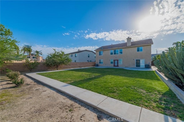 back of house featuring a fenced backyard, a lawn, stucco siding, a chimney, and a patio area