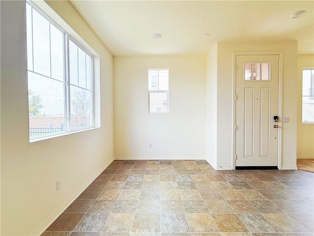 foyer with a wealth of natural light, stone finish floor, and baseboards