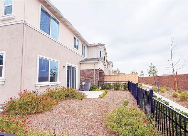 view of side of home featuring fence, central AC, and stucco siding