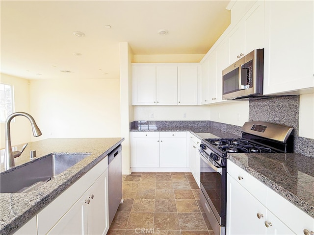 kitchen with dark stone counters, stainless steel appliances, a sink, and white cabinets