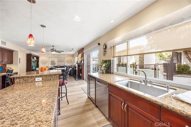 kitchen featuring a breakfast bar area, light wood-style flooring, a sink, dishwasher, and decorative light fixtures