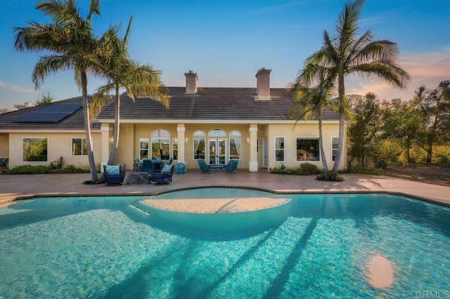 back of property at dusk with a patio, a chimney, stucco siding, and an outdoor pool