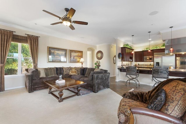 living room with arched walkways, carpet floors, crown molding, baseboards, and ceiling fan