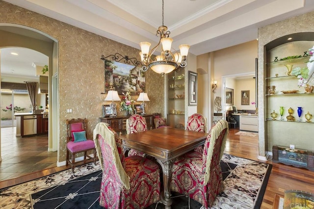 dining room with ornamental molding, wood finished floors, arched walkways, a notable chandelier, and a raised ceiling