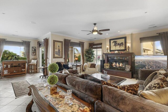 living area with visible vents, a ceiling fan, a glass covered fireplace, crown molding, and light tile patterned floors