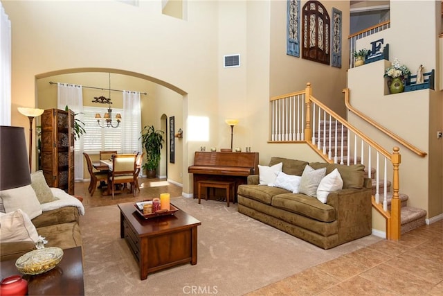 tiled living room featuring baseboards, visible vents, an inviting chandelier, arched walkways, and stairs