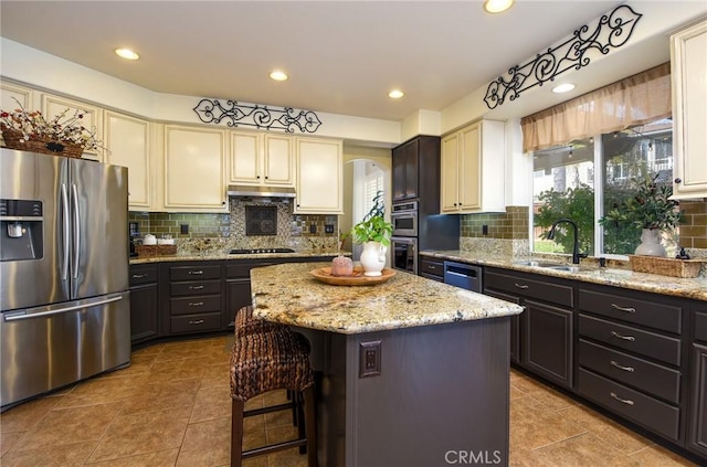 kitchen featuring a sink, under cabinet range hood, tasteful backsplash, a kitchen island, and stainless steel appliances
