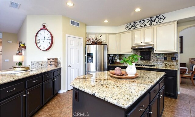 kitchen featuring visible vents, stainless steel fridge with ice dispenser, cream cabinetry, under cabinet range hood, and tasteful backsplash