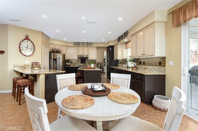 kitchen featuring visible vents, tasteful backsplash, stainless steel fridge, light tile patterned floors, and light stone countertops