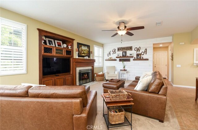 living area with a fireplace with flush hearth, a ceiling fan, baseboards, and light tile patterned floors
