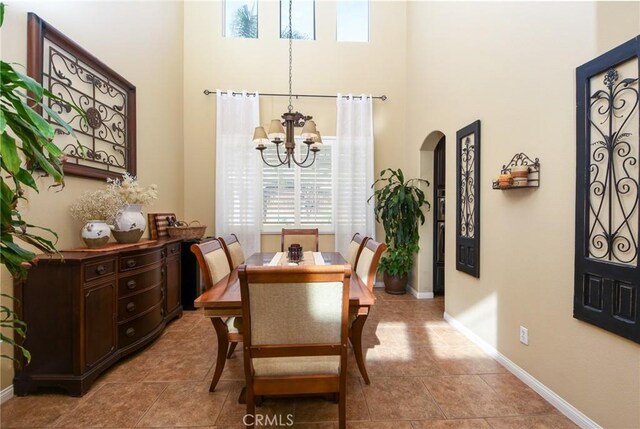 dining space featuring baseboards, arched walkways, a towering ceiling, and a chandelier