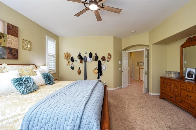 bedroom with arched walkways, light colored carpet, a ceiling fan, and baseboards