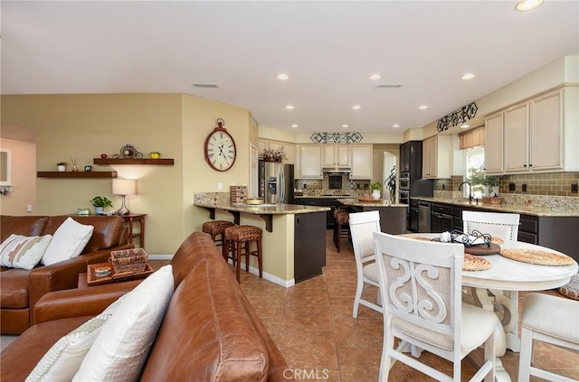 kitchen featuring tasteful backsplash, visible vents, a breakfast bar, a peninsula, and stainless steel fridge
