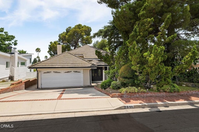 view of front of home with a garage, concrete driveway, a chimney, and a tile roof