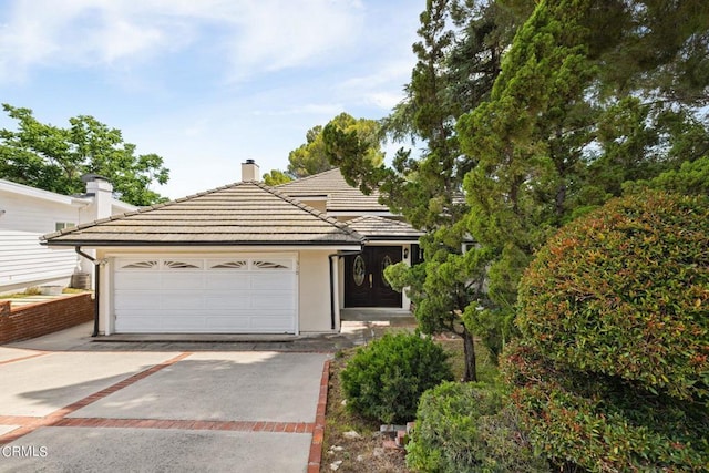 view of front facade featuring a chimney, concrete driveway, a tiled roof, and a garage