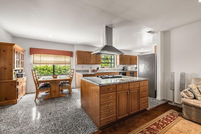 kitchen featuring visible vents, brown cabinetry, a center island, range hood, and stainless steel appliances