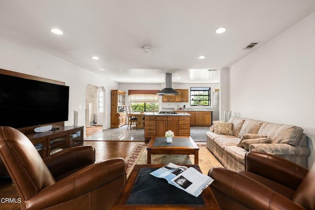 living room featuring arched walkways, recessed lighting, visible vents, and light wood-style flooring