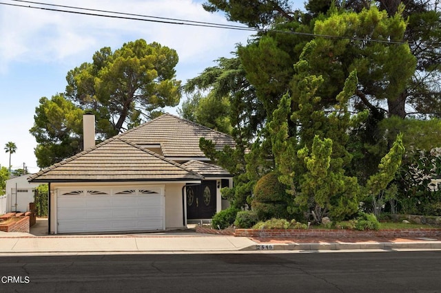 view of front facade featuring a garage, a tile roof, concrete driveway, stucco siding, and a chimney