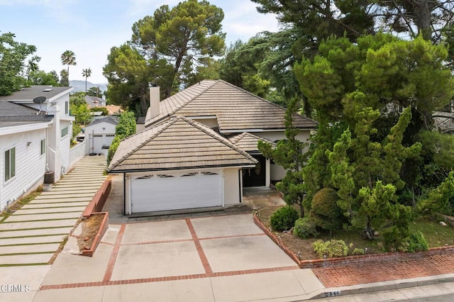 view of front facade with a garage, concrete driveway, a chimney, and a tiled roof