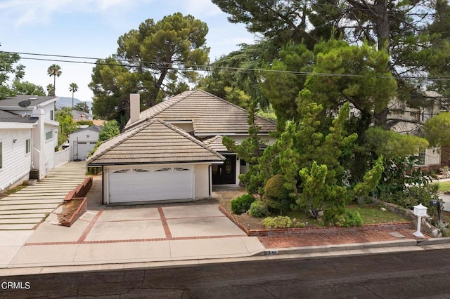 view of front facade with concrete driveway, a chimney, an attached garage, and a tile roof