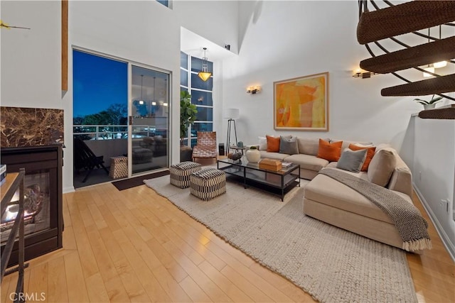 living area with a high ceiling, wood finished floors, a glass covered fireplace, and baseboards