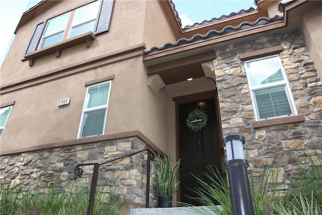 entrance to property featuring stone siding, a tile roof, and stucco siding