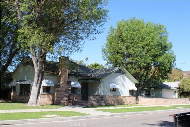 single story home with a chimney, stucco siding, a front yard, a garage, and stone siding