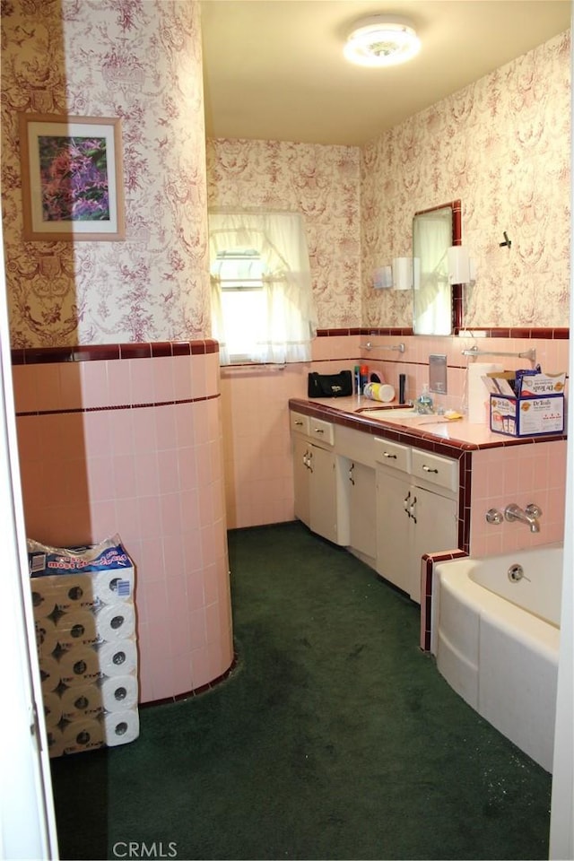 bathroom with a tub to relax in, tile walls, wainscoting, vanity, and wallpapered walls