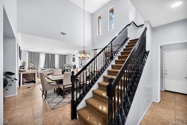 staircase with baseboards, visible vents, a towering ceiling, tile patterned floors, and a notable chandelier